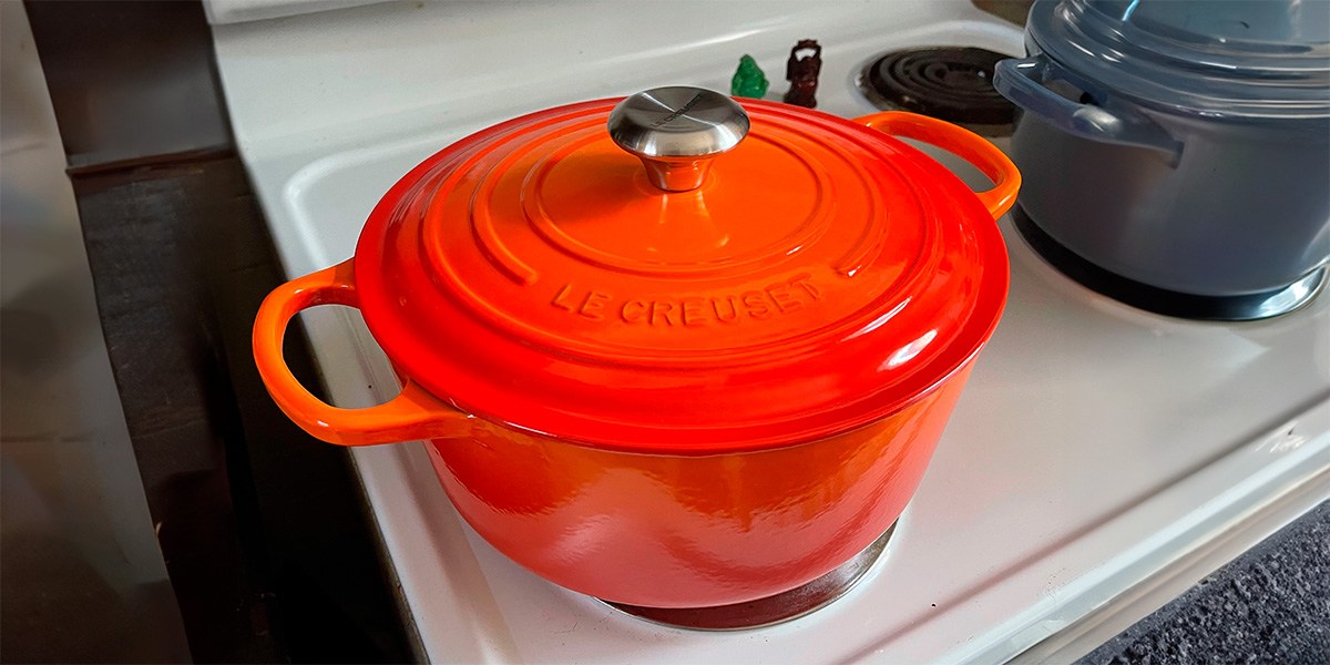 Bright orange Le Creuset Round Dutch Oven on stovetop burner Bright orange Le Creuset Round Dutch Oven on stovetop burner