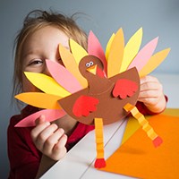 Child holding up arts and crafts turkey with feathers